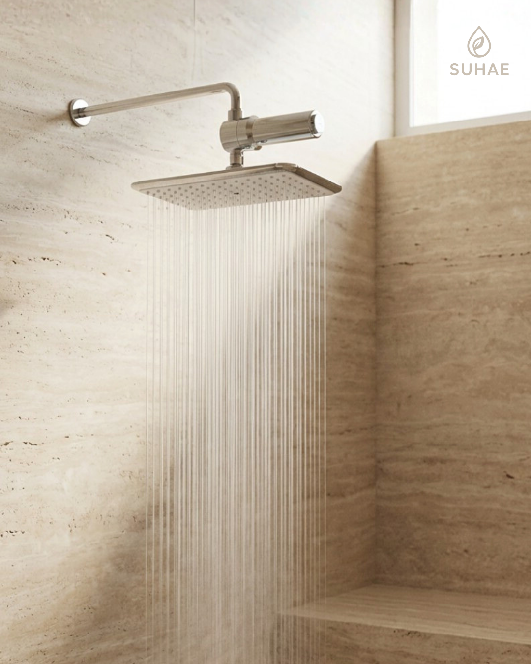 A Suhae overhead shower system on a travertine wall, water falling as fine parallel lines.